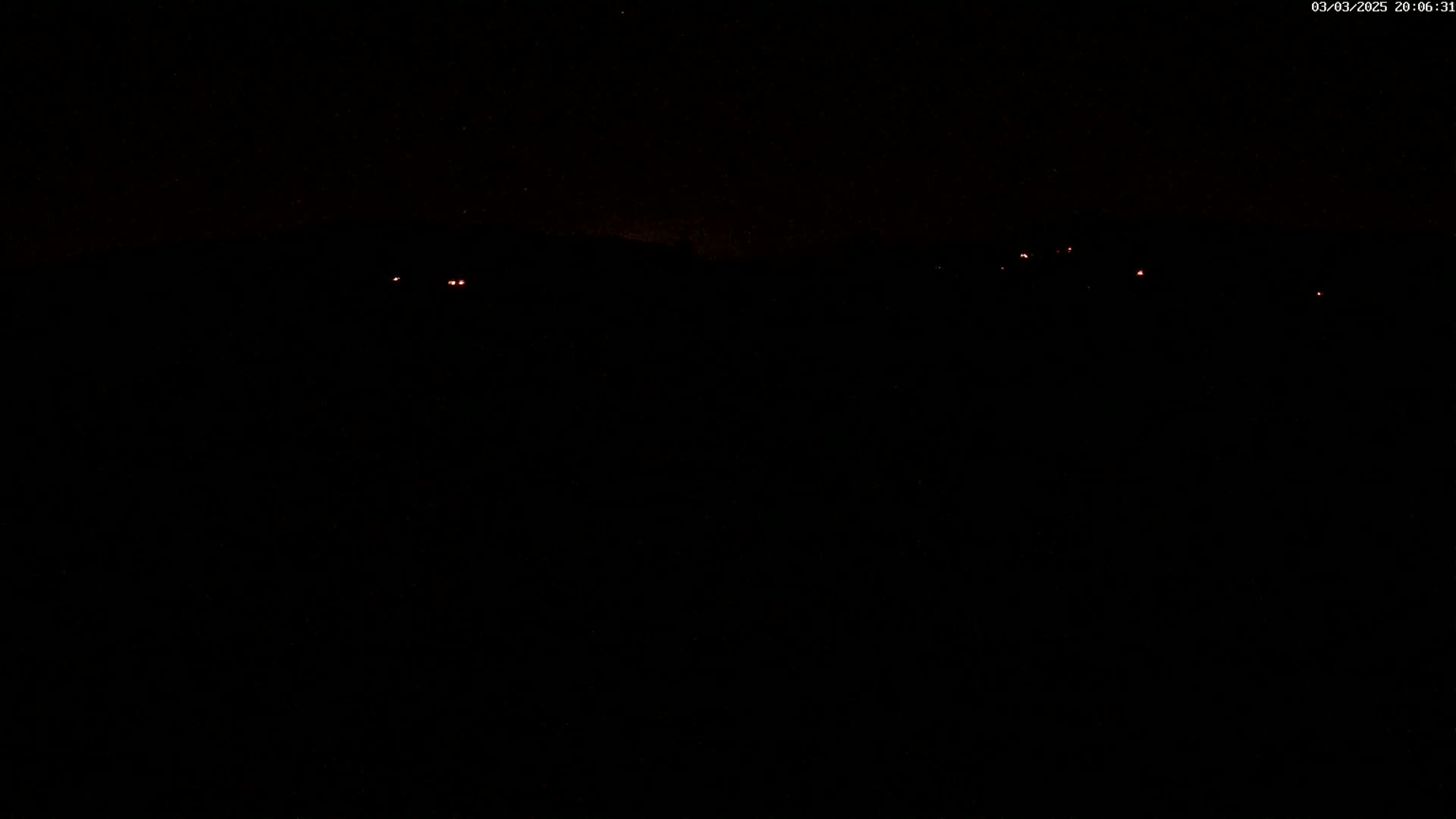 A dark, nighttime scene with a few faint, distant red lights visible on the horizon.