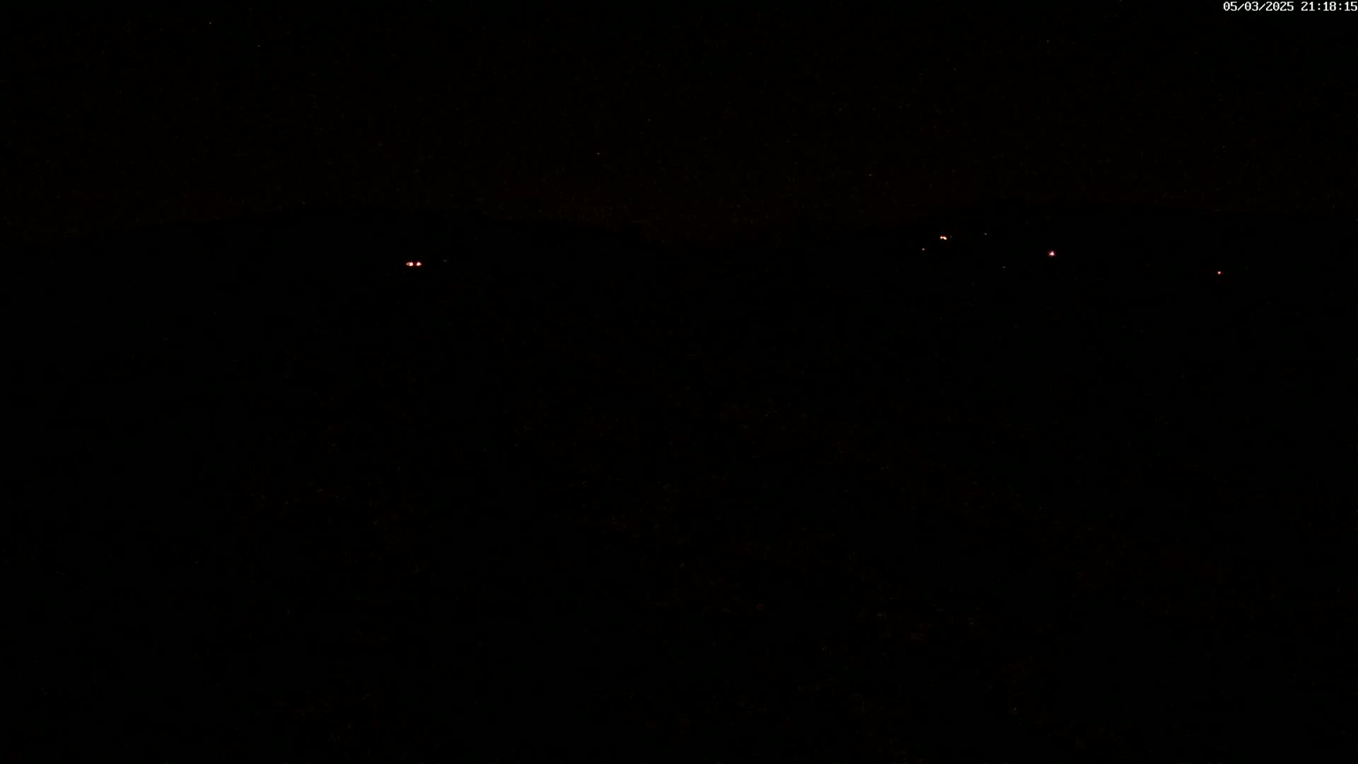 A dark, nighttime scene shows several faint red lights in the distance under a clear, starlit sky.
