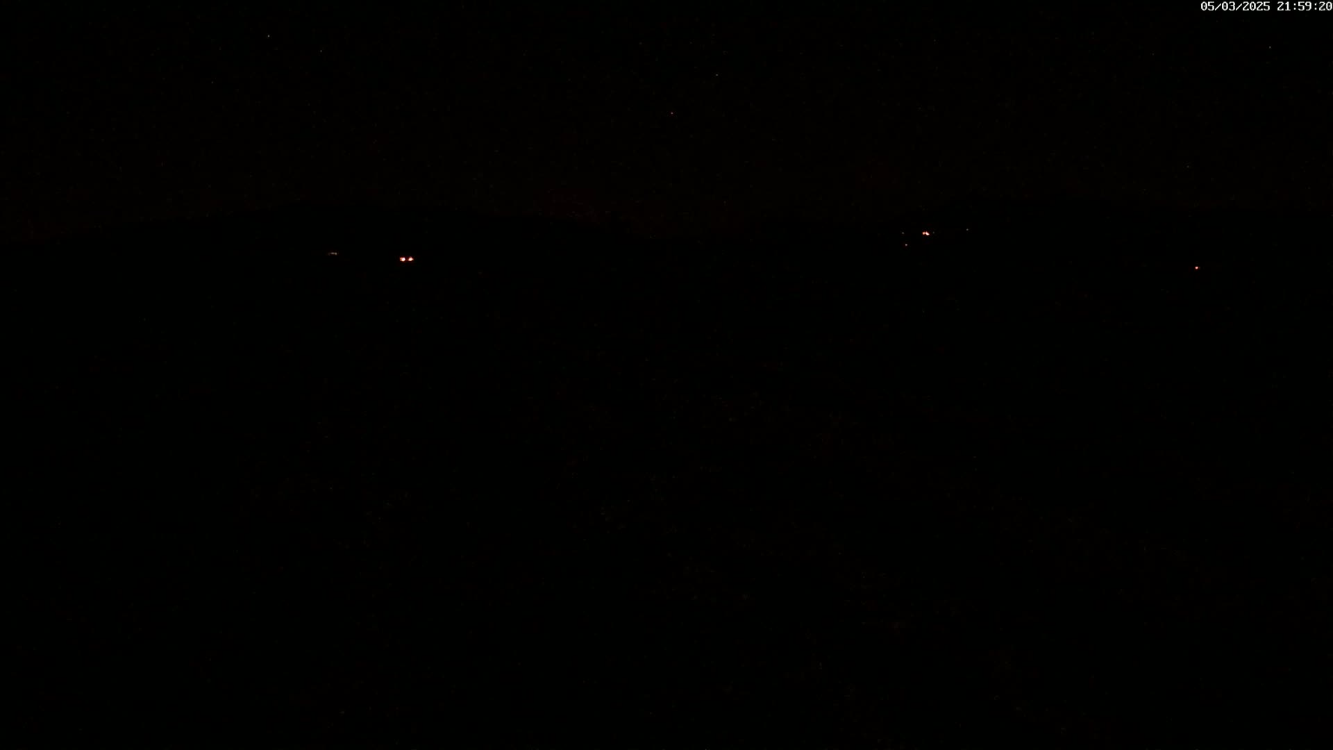 A dark, nighttime scene with a few faint, distant lights visible against a black sky.