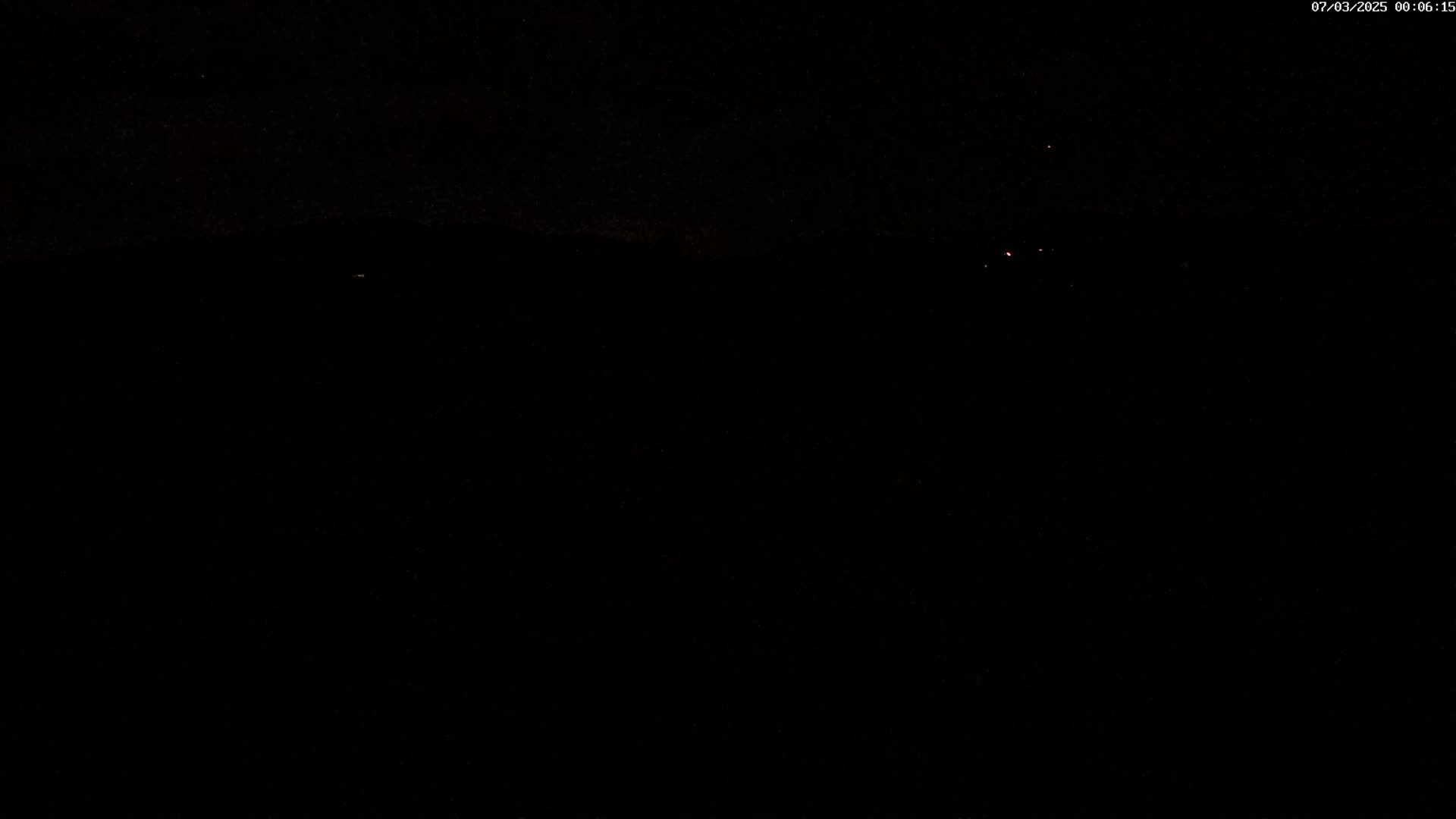 A dark, nighttime scene shows a few distant, faint lights against a completely black background.