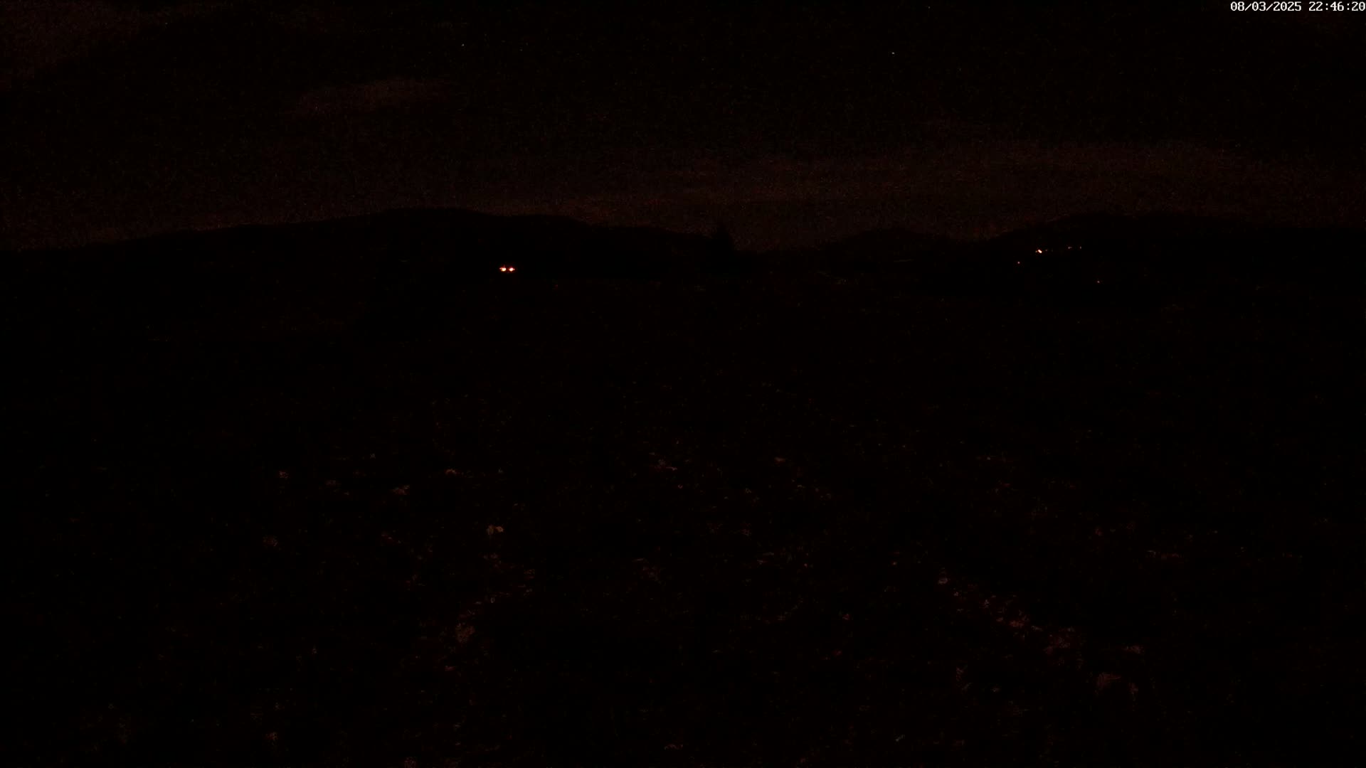 At night, two pairs of distant headlights are visible in the dark landscape, under a mostly clear sky.
