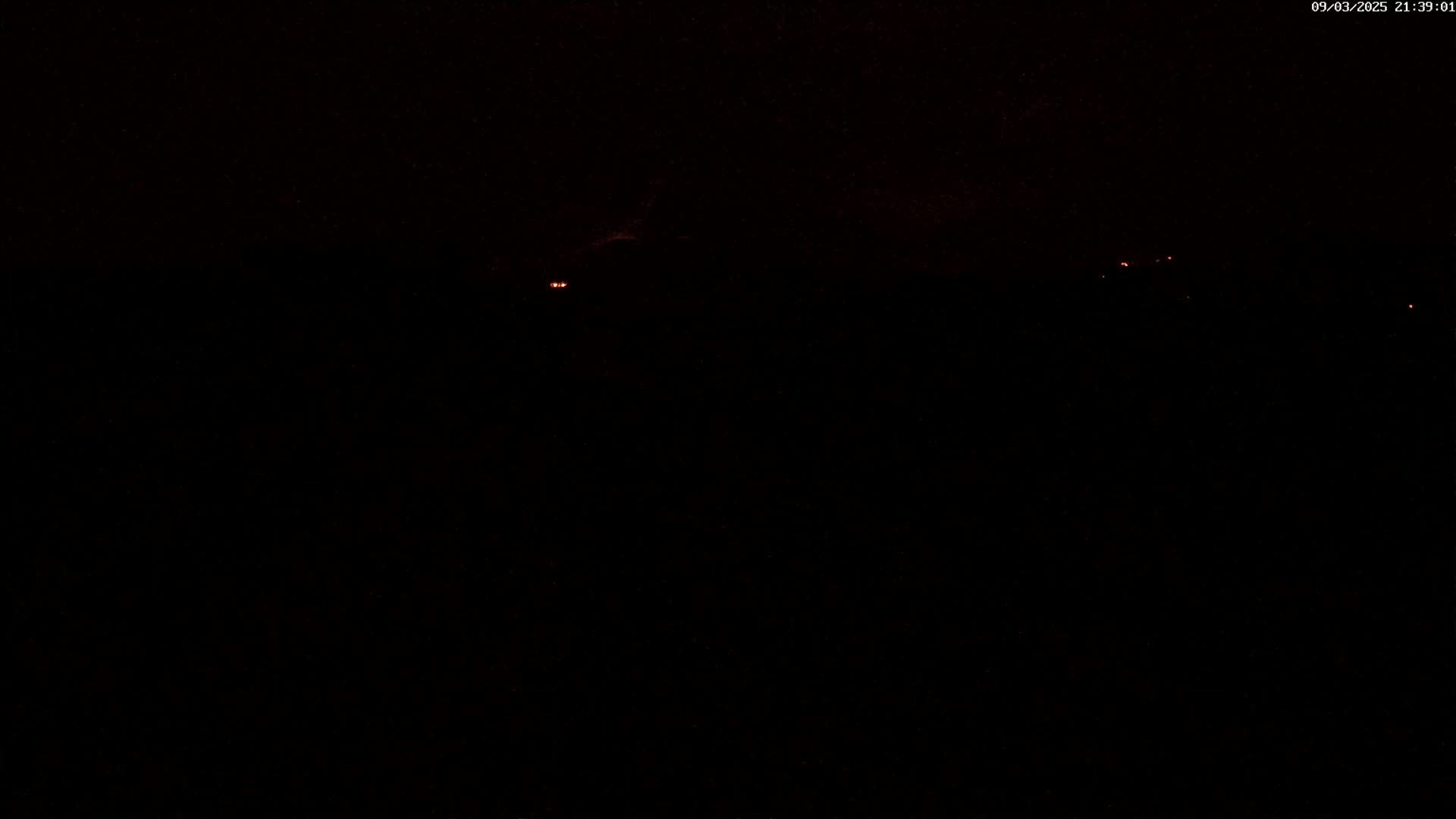 A dark, nighttime scene shows a few faint, distant lights against a mostly black sky.