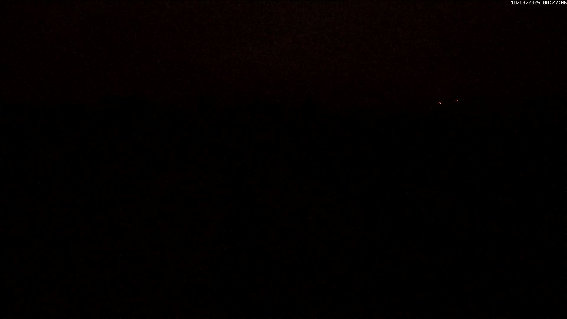 A dark nighttime scene with two faint reddish lights visible in the distance.