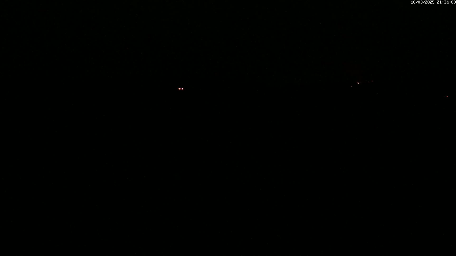A dark, nighttime scene shows a few faint red lights in the distance.