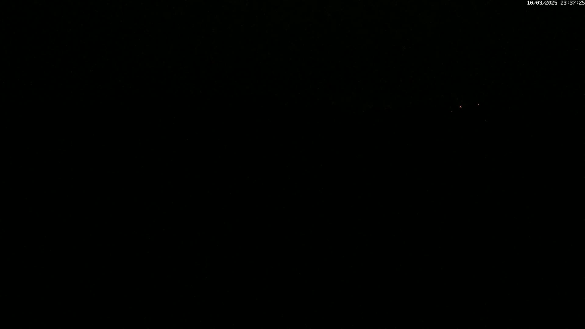 A mostly black image shows a few faint, distant red lights at night.