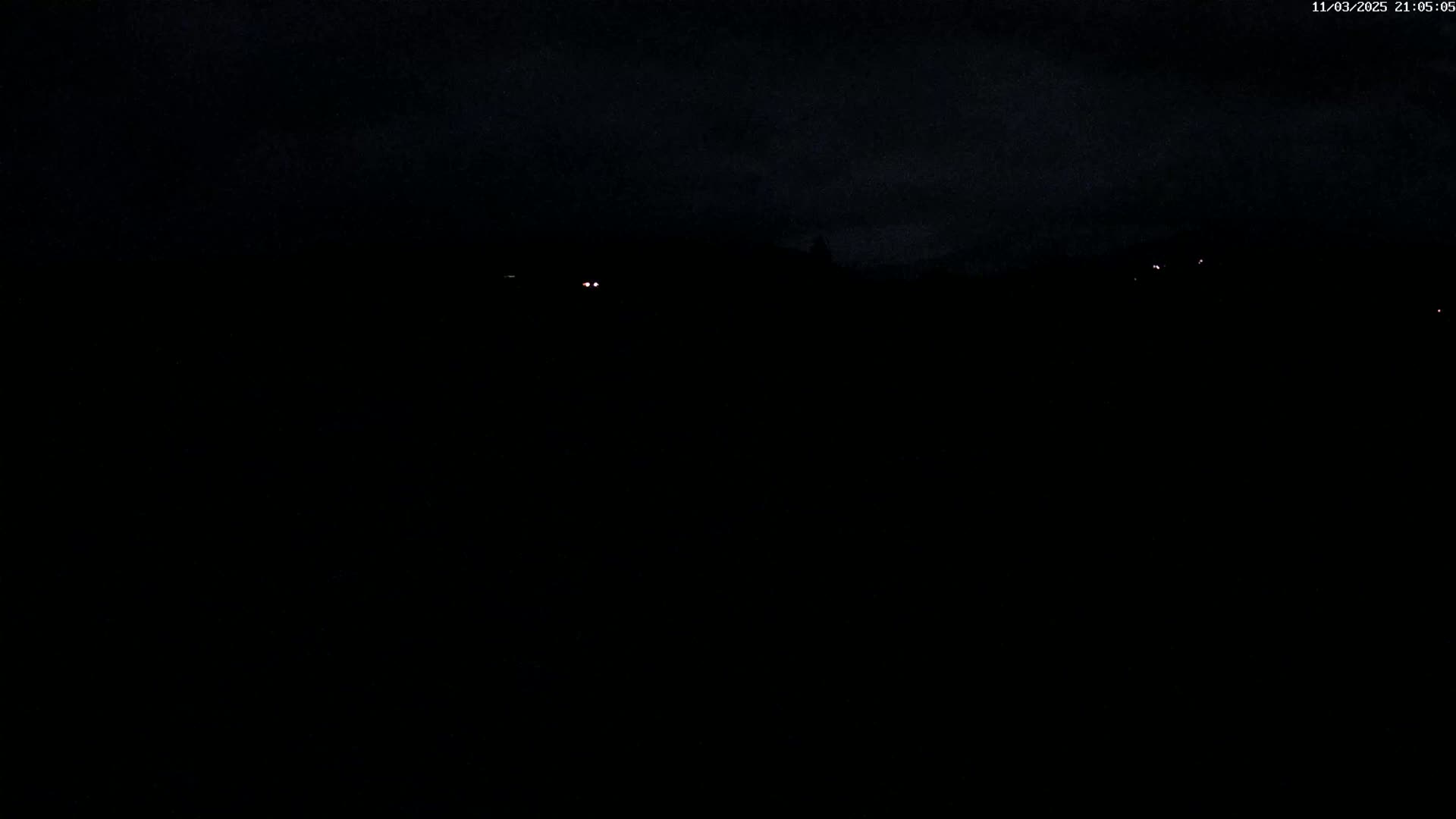 A dark, nighttime scene shows a few faint lights in the distance under a cloudy sky.