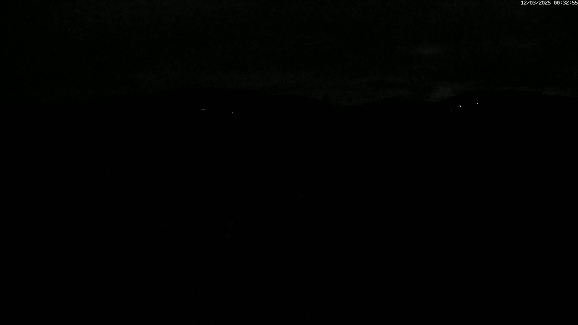 A dark, nighttime scene shows a few faint lights in the distance under a mostly clear sky.