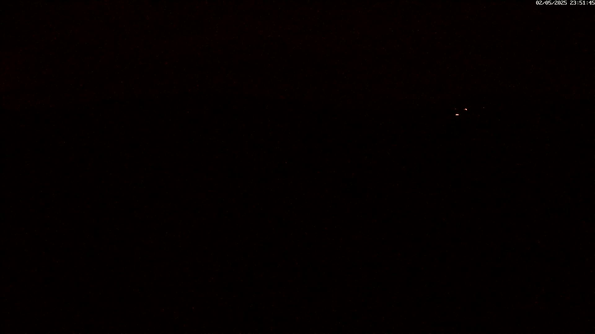 A dark, nighttime scene with a few faint, reddish lights visible in the distance.
