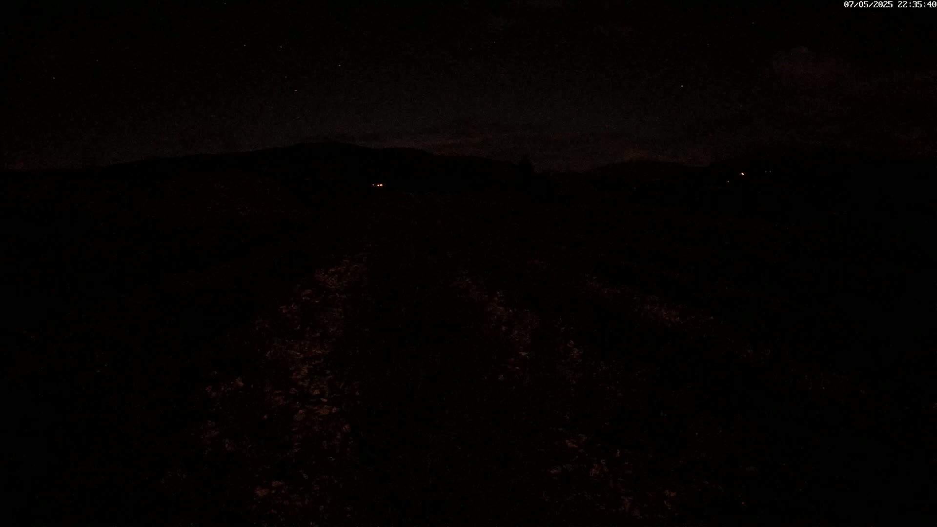 A dark, nighttime landscape with a few faint lights in the distance under a starry sky.