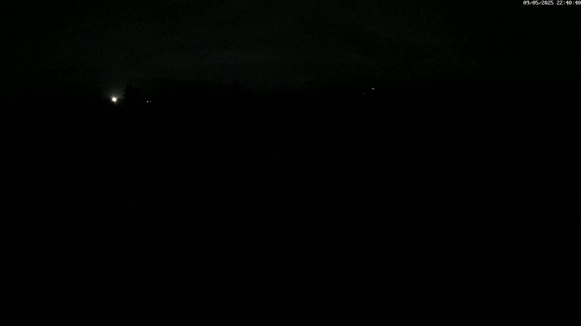A dark, nighttime scene shows a few faint lights in the distance under a mostly clear sky.