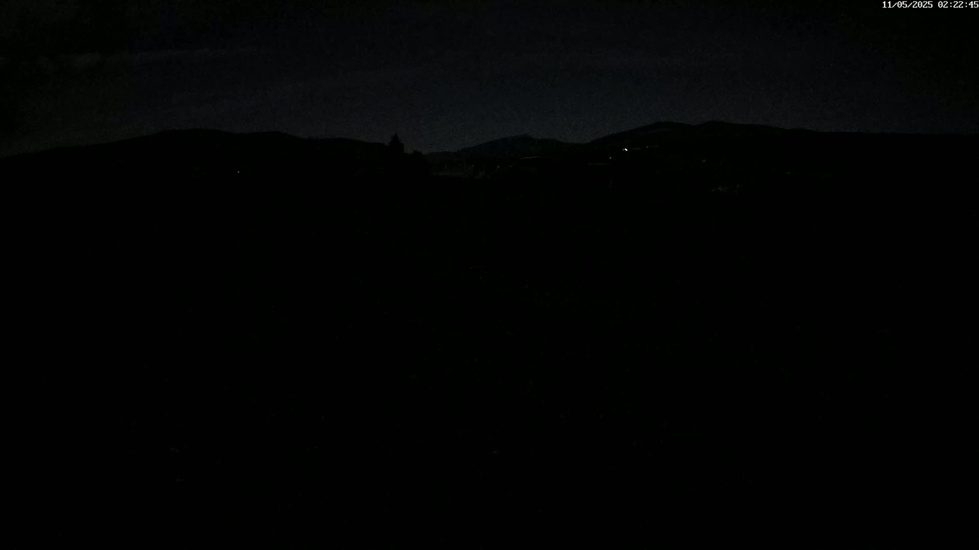 A dark, nighttime landscape shows a distant, silhouetted mountain range under a mostly clear sky.