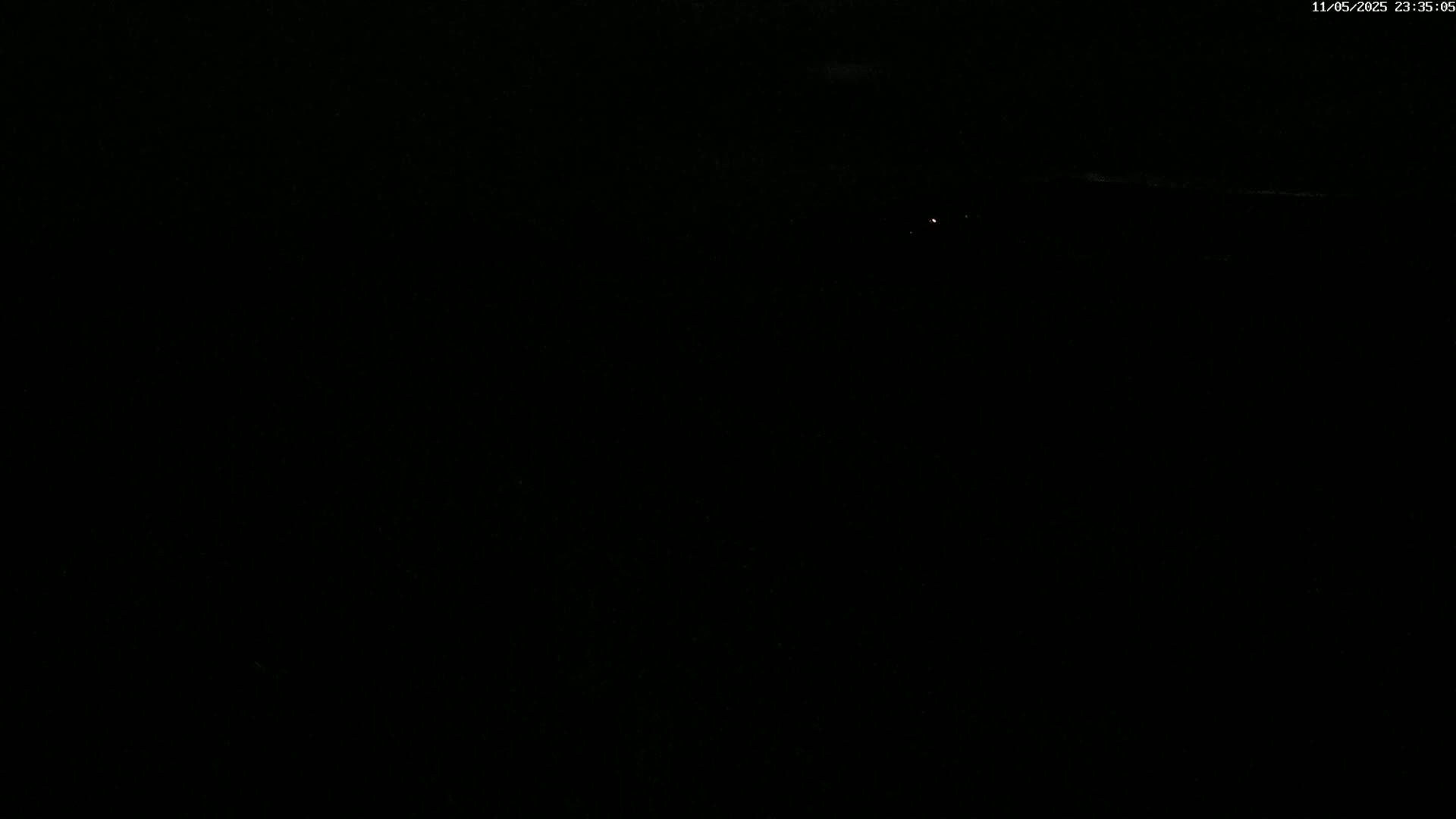 A dark nighttime scene shows a faint, distant light source on a dark horizon.