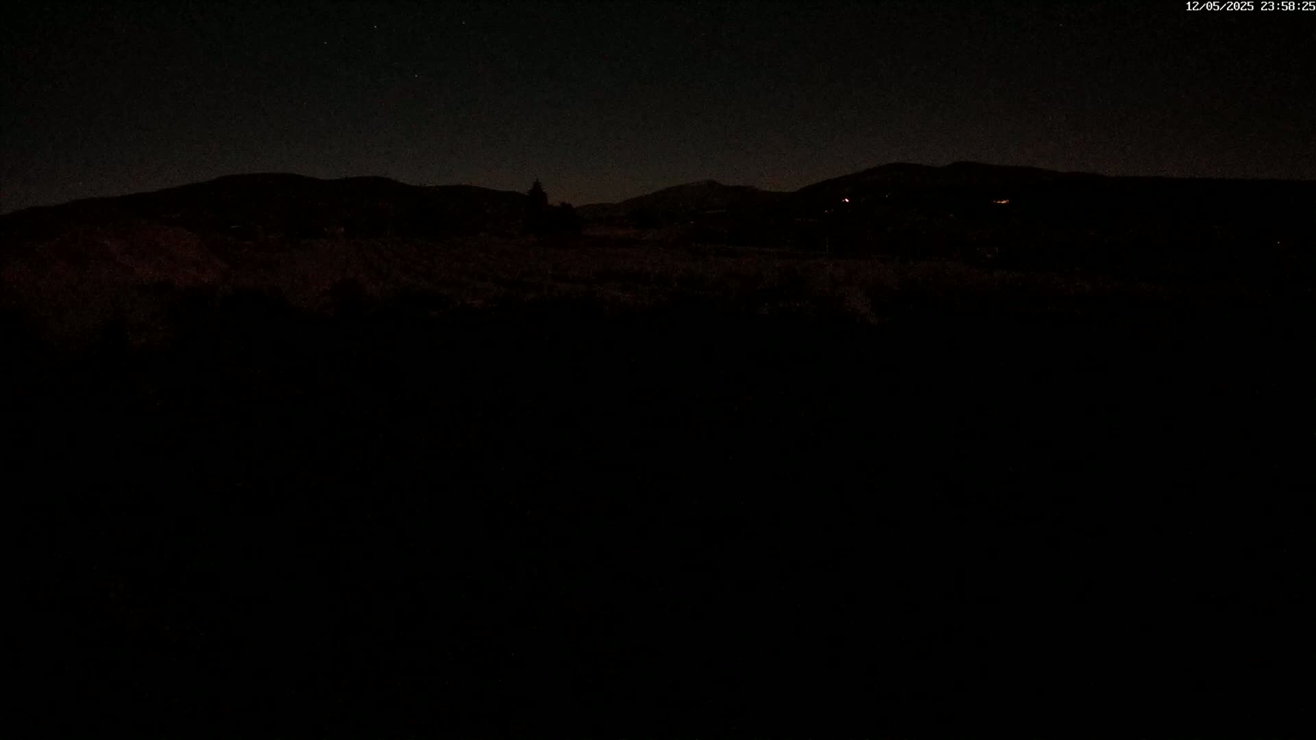 A dark, nighttime landscape shows a silhouetted line of hills under a clear, starry sky.