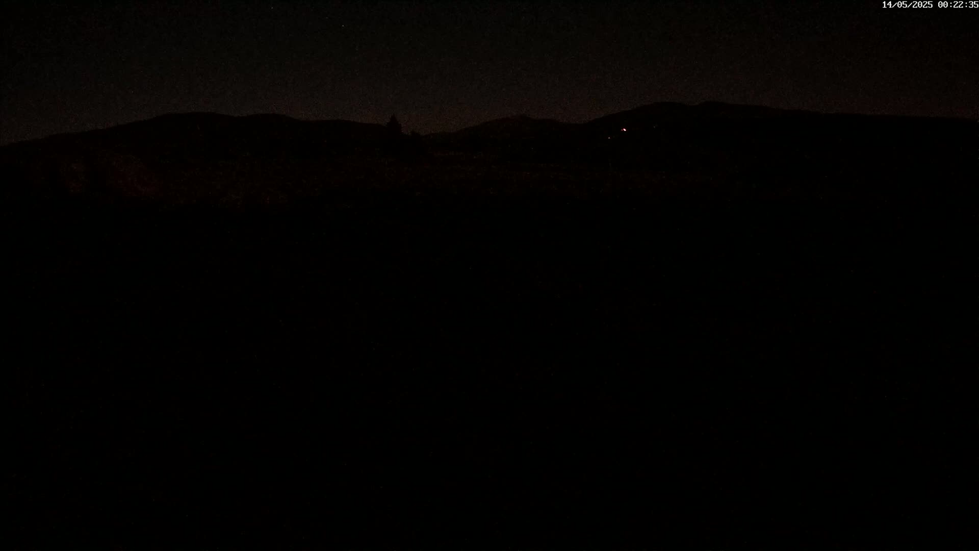 A dark, nighttime scene shows a silhouetted mountain range under a clear, starlit sky.