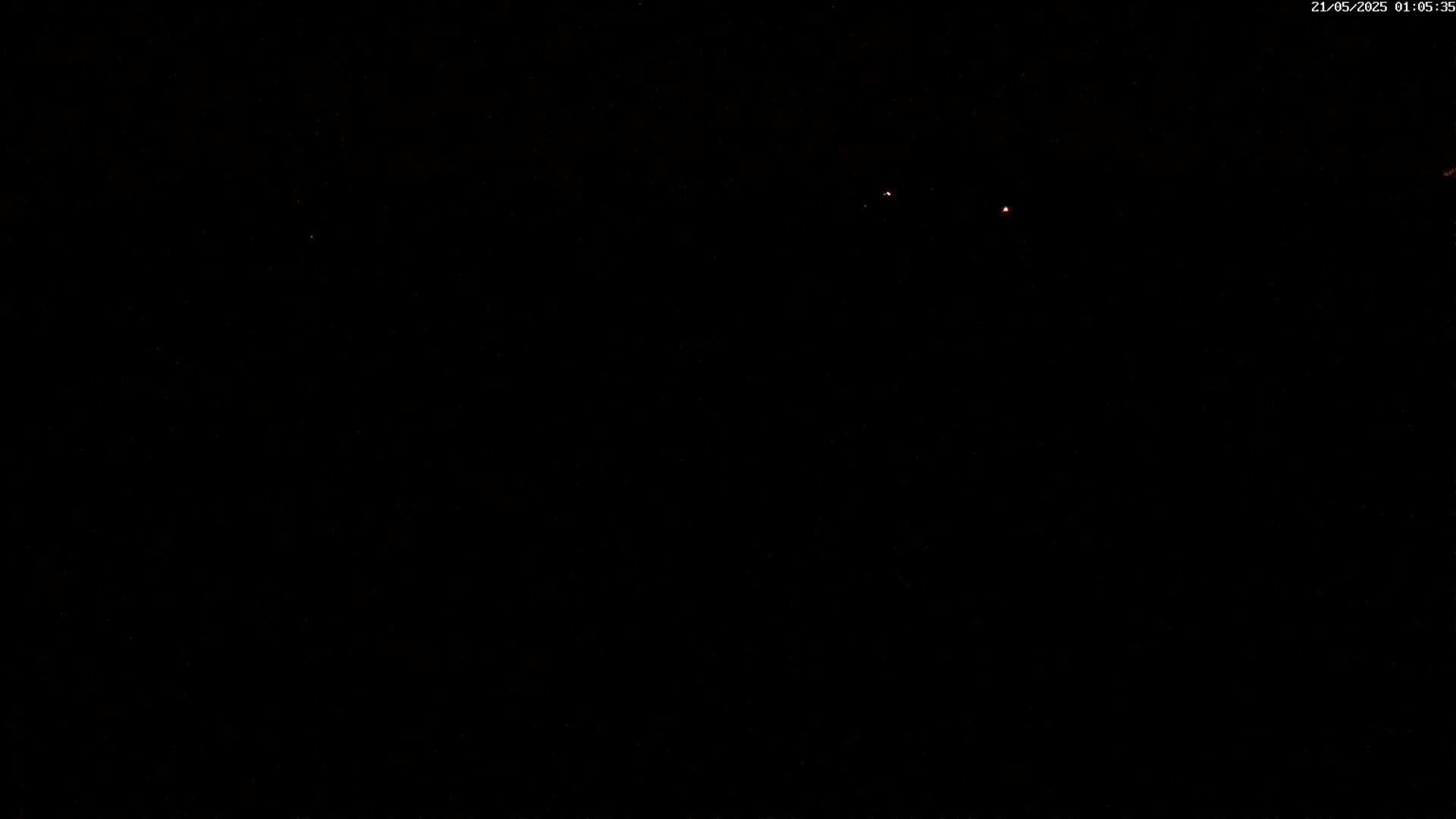 A mostly dark image shows a few faint orange lights in the distance under a clear night sky.
