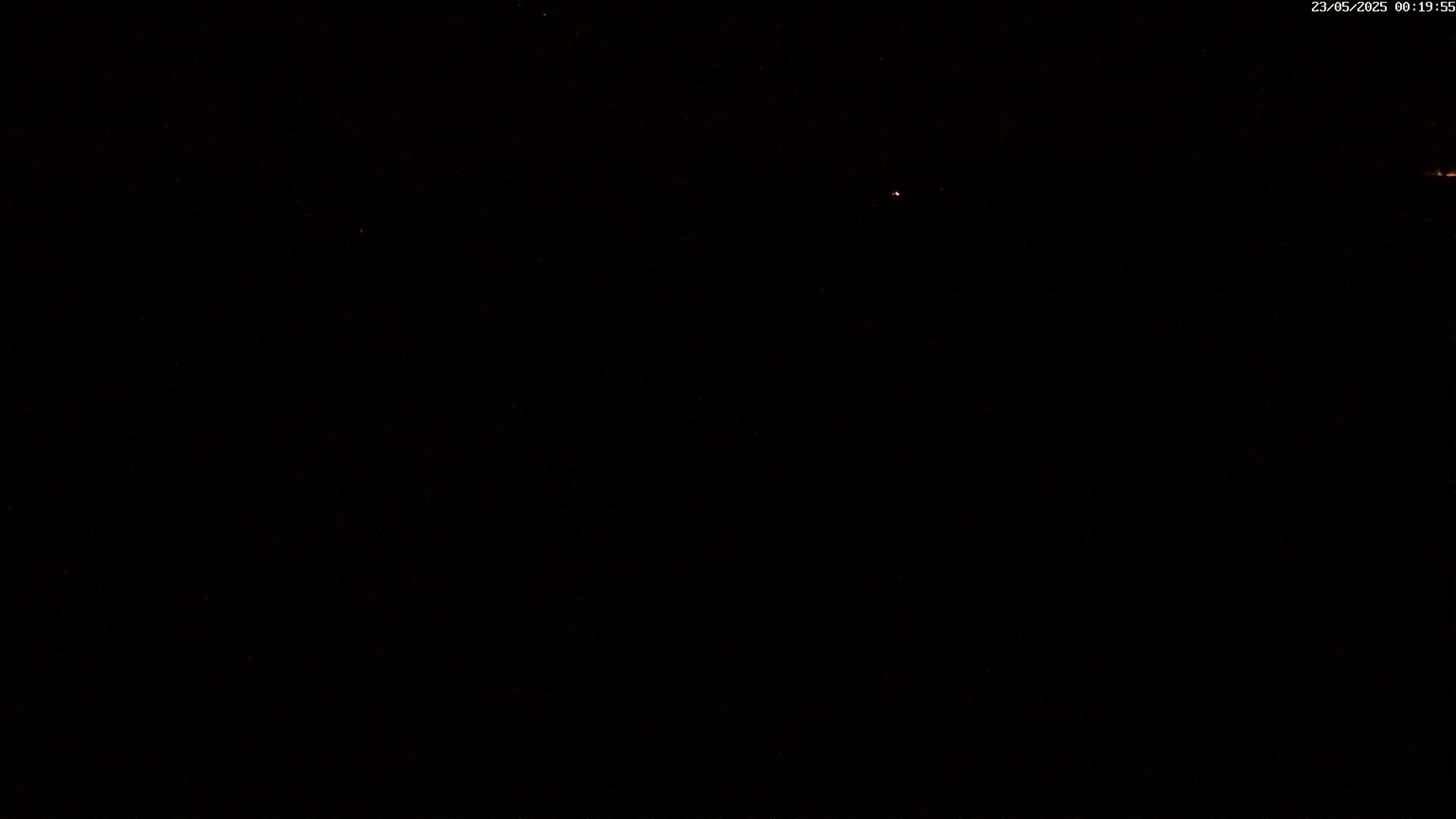 A dark nighttime scene shows a few faint lights in the distance under a clear, star-filled sky.