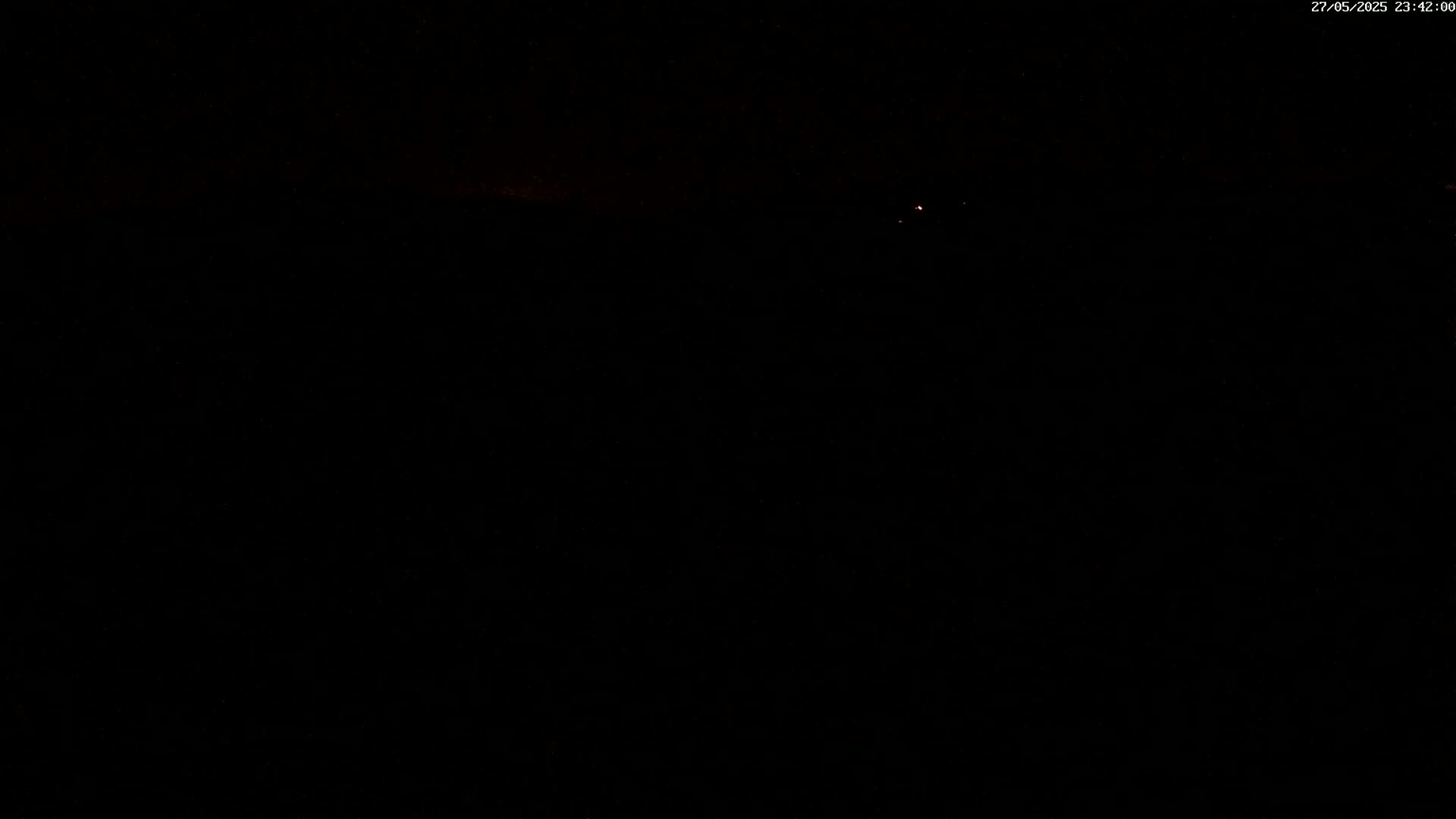 A very dark night scene shows a few faint red lights in the distance.