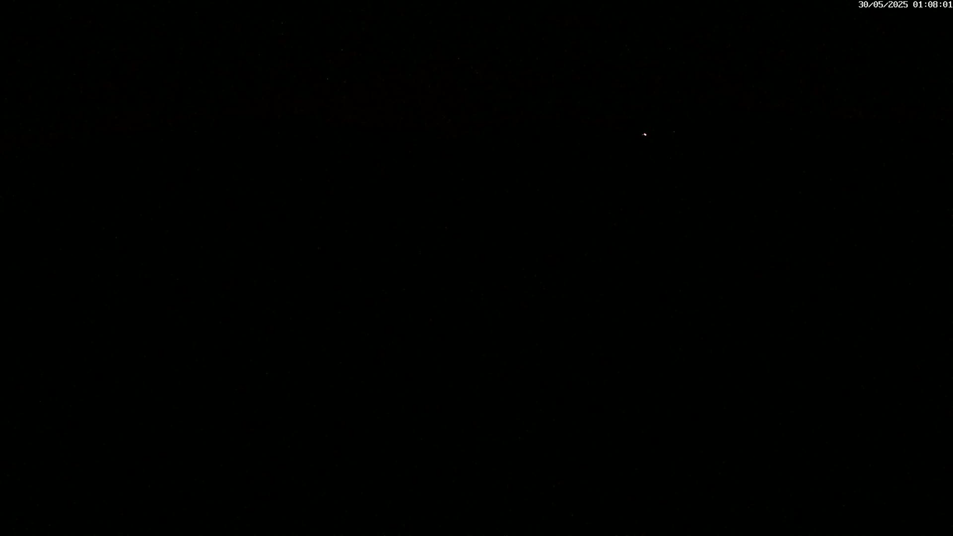 A single, faint light is visible in a pitch-black night sky.