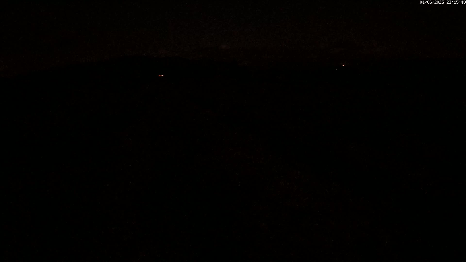 A mostly dark, nighttime scene shows a few faint orange lights in the distance.