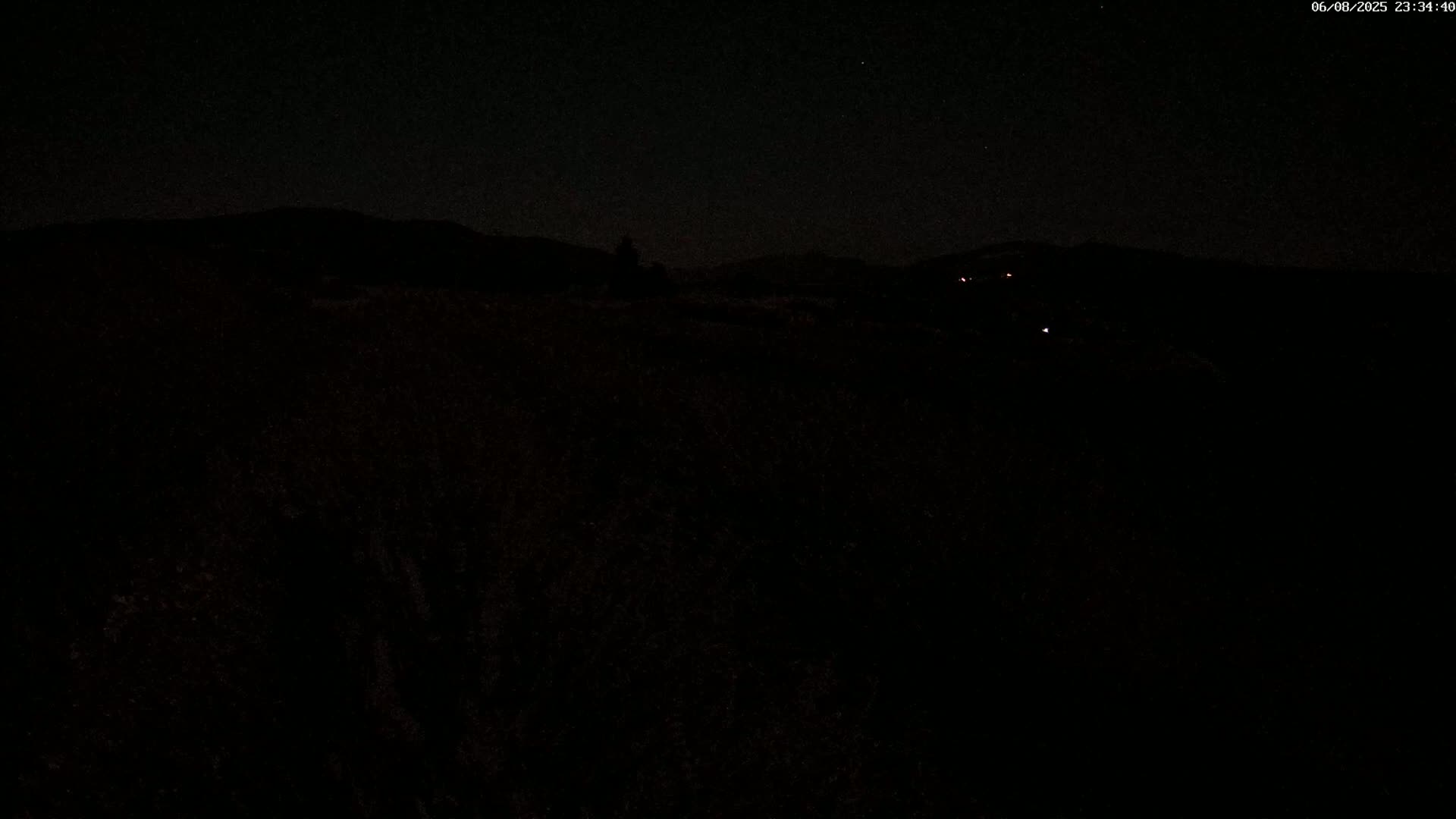 A nighttime view of dark, silhouetted hills under a clear, starlit sky.