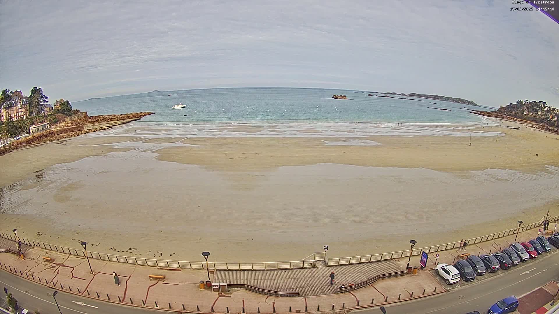 An expansive sandy beach stretches out to a calm sea under a cloudy sky, with a boardwalk and parked cars lining the shore.