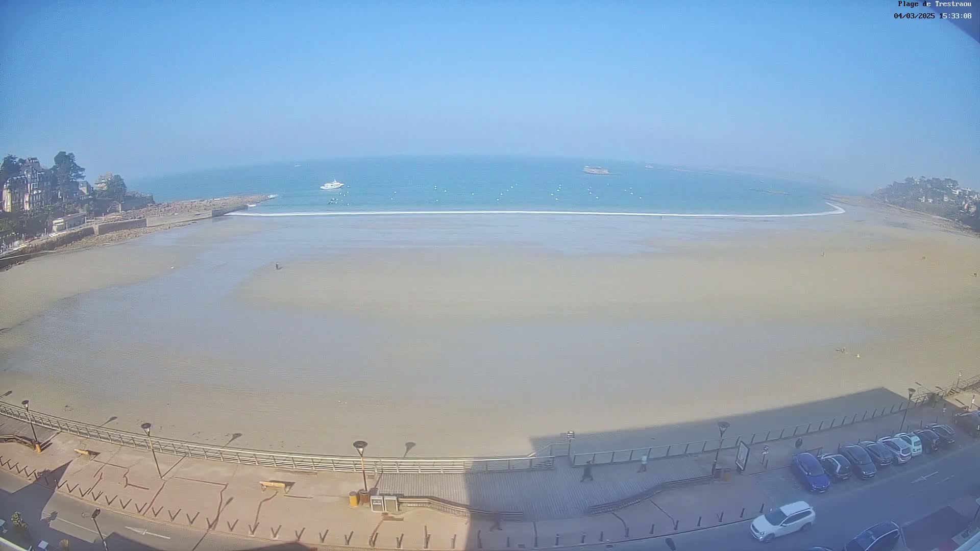A wide, sandy beach stretches out to a calm, light-blue ocean under a clear, bright sky.