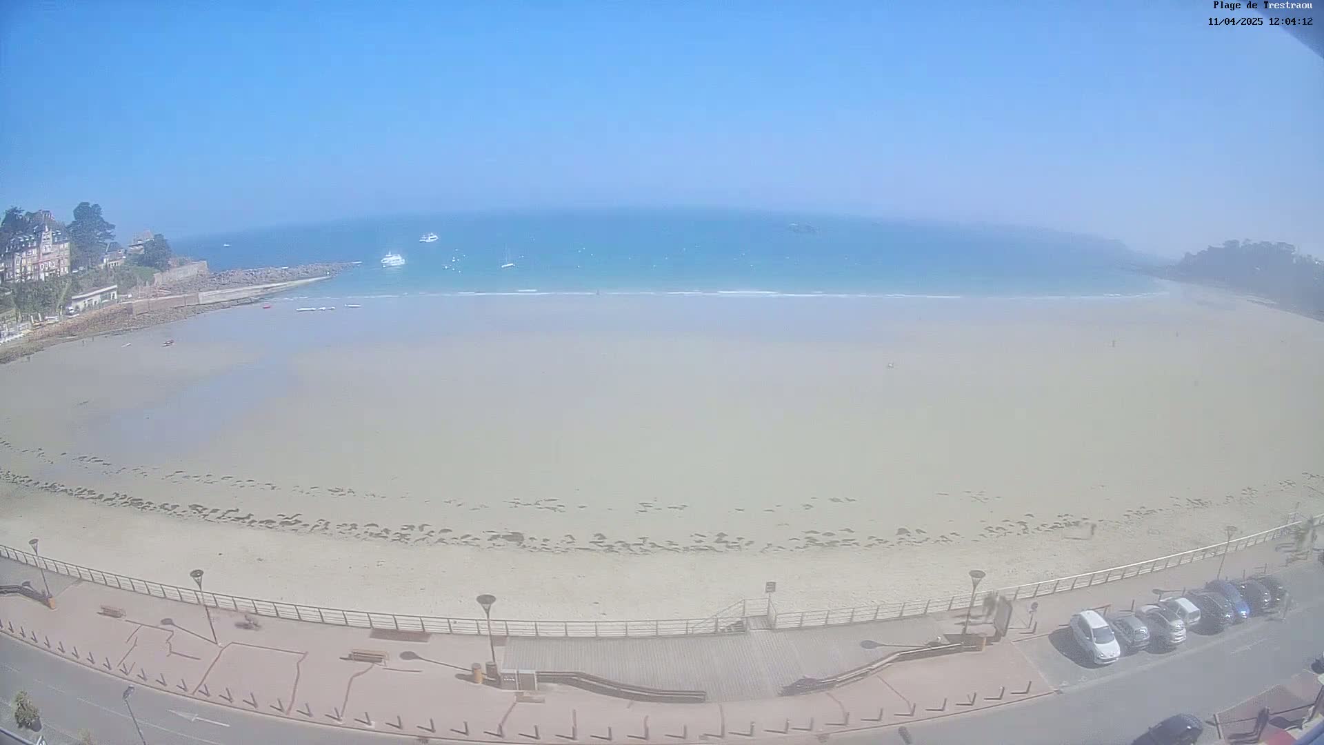 An expansive sandy beach with a few people and several boats on the ocean, under a clear blue sky.