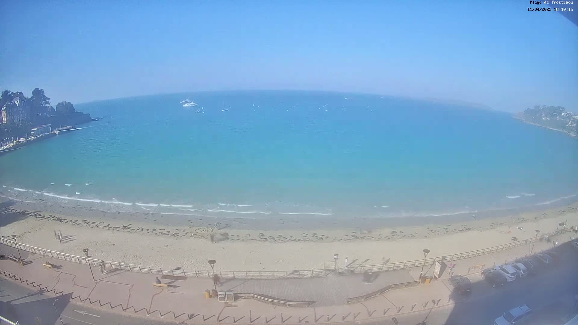 A sandy beach with light waves laps at the shore of a clear, turquoise ocean under a bright, sunny sky.