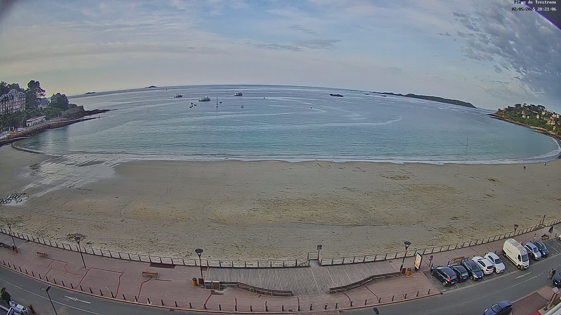 A mostly sandy beach curves around a calm, light-blue bay under a partly cloudy sky.