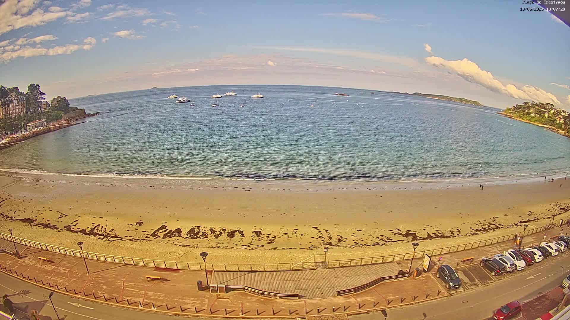A sandy beach with several boats in the distance is seen on a partly sunny day.
