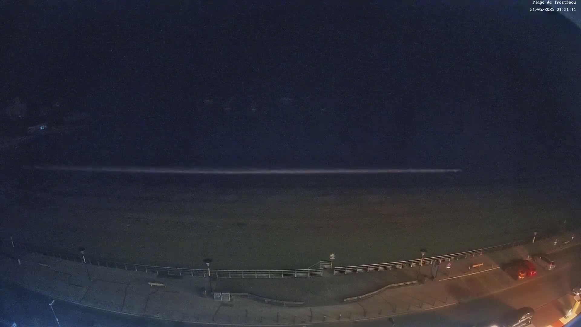 A nighttime, long-exposure shot shows a dark beach and ocean with a long, thin streak of light across the water under a dark sky.