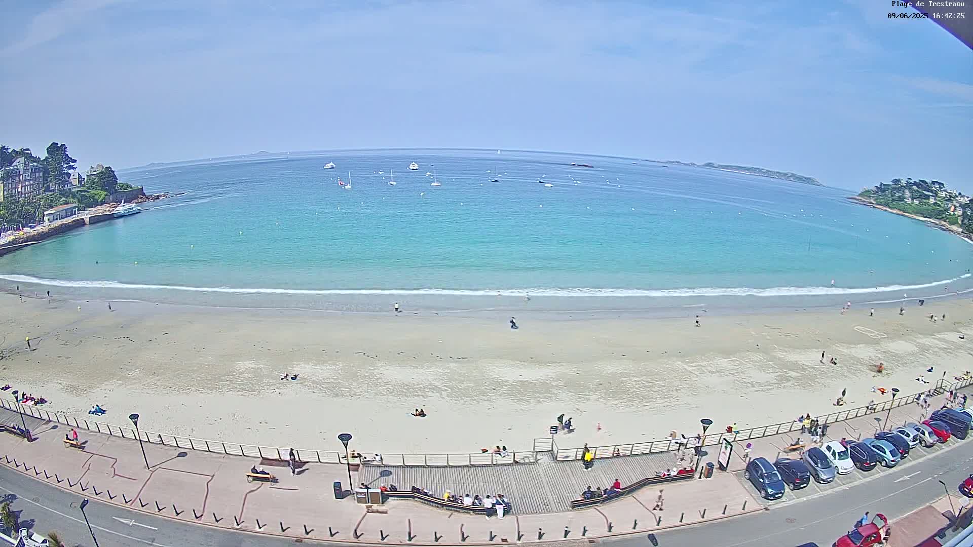 A sandy beach with turquoise water and several people on it, under a clear blue sky, is viewed from above.