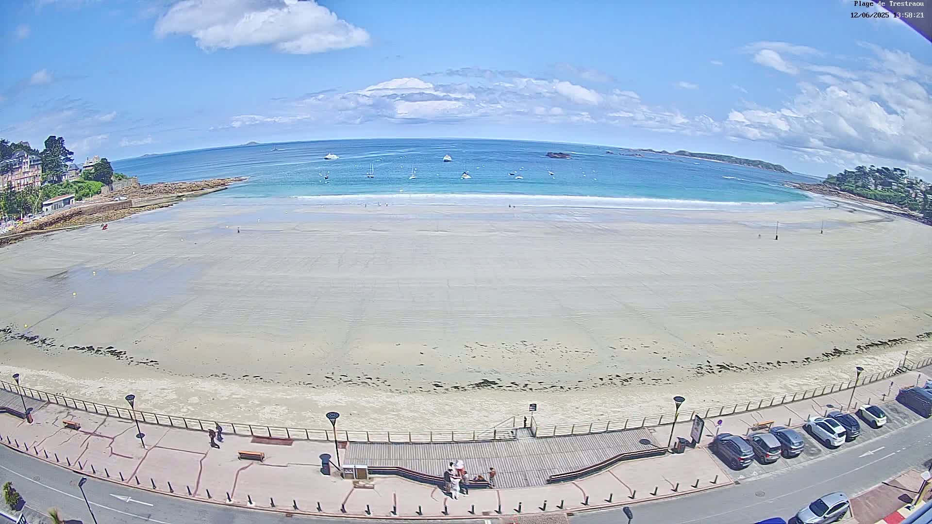 A mostly empty sandy beach stretches out to a calm, turquoise ocean under a partly cloudy sky.