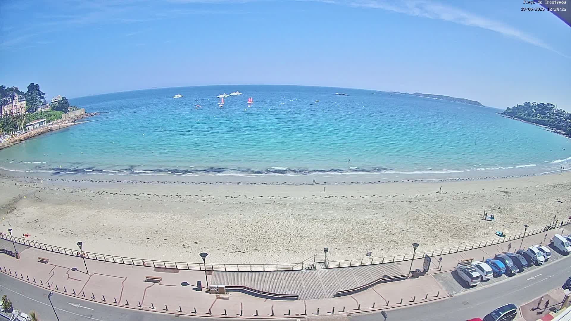 A sandy beach with turquoise water and several boats visible on a sunny day.