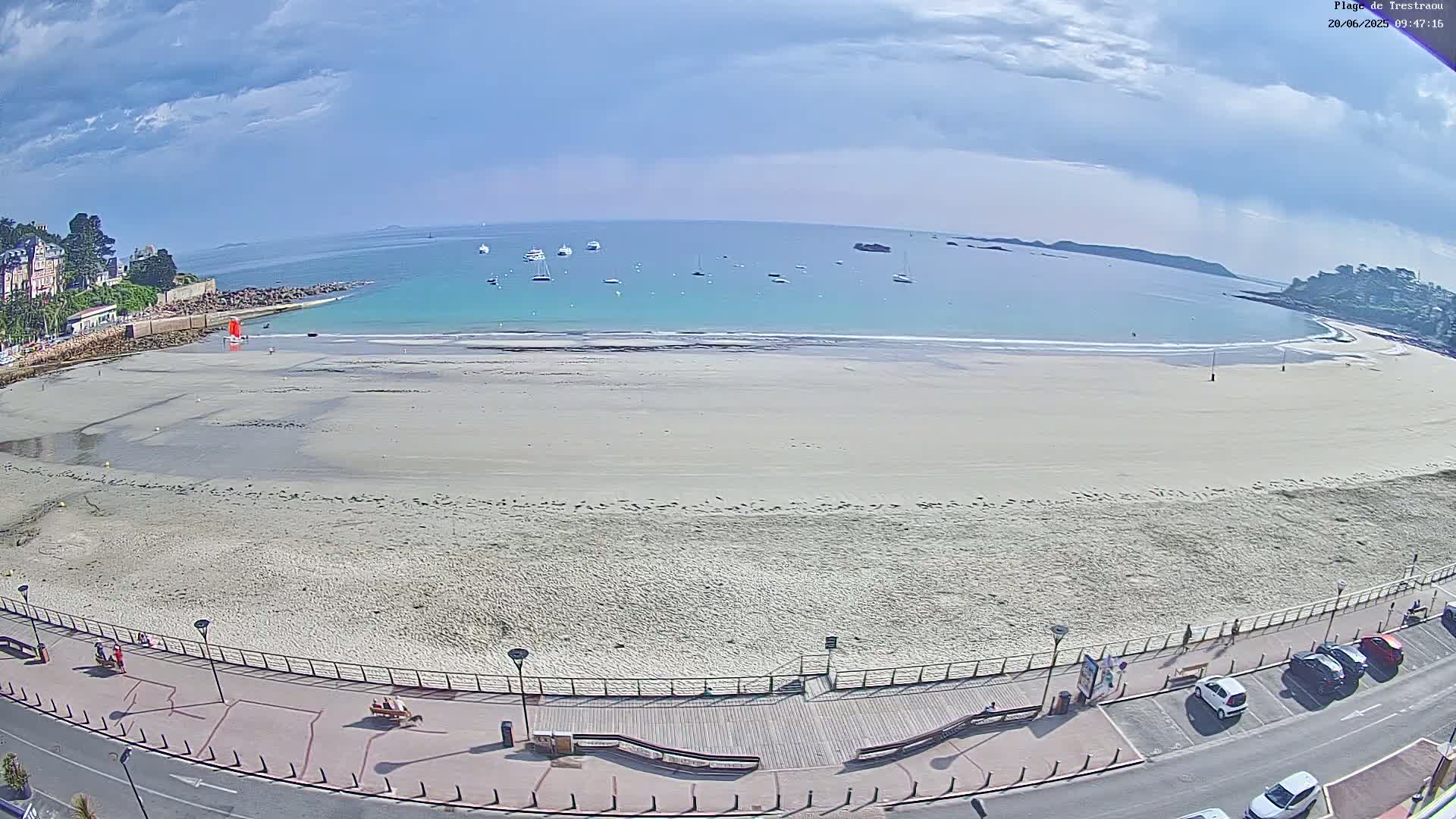 A wide sandy beach with calm, light-blue water and several boats is visible under a mostly clear sky.