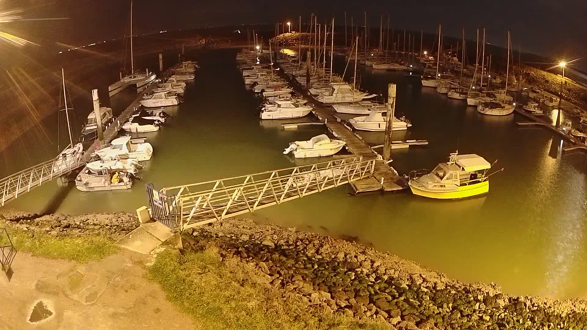 A marina at night, filled with numerous boats moored alongside docks, is illuminated under a dark sky.