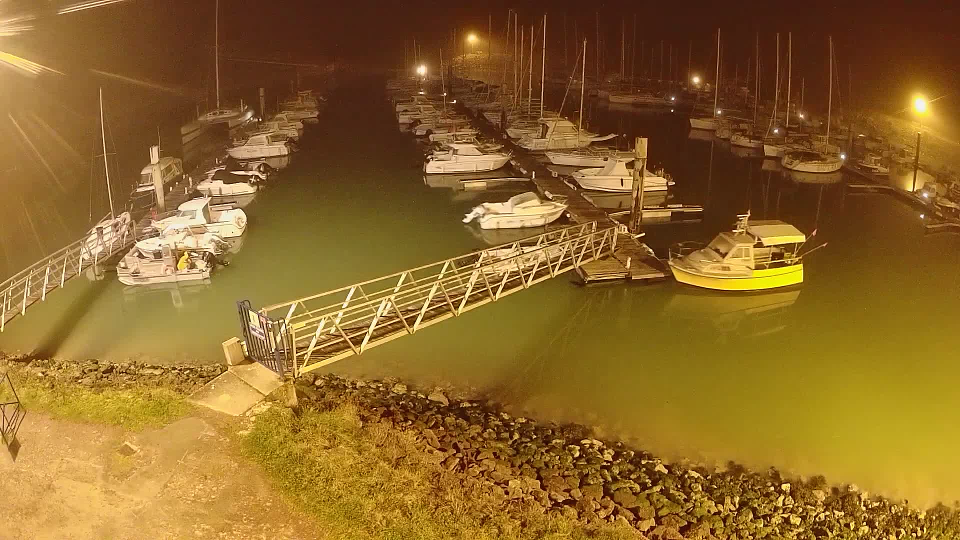 A marina at night, shrouded in fog, contains numerous boats moored at docks connected by a metal gangway.