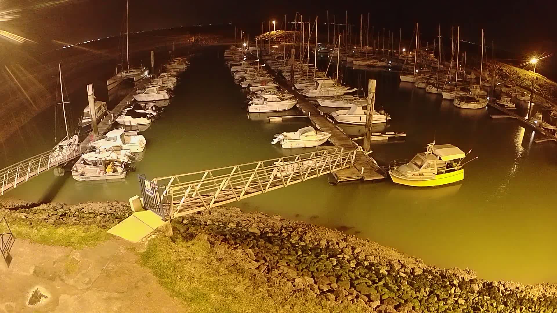 A marina at night, filled with numerous boats docked along piers, under dimly lit conditions.