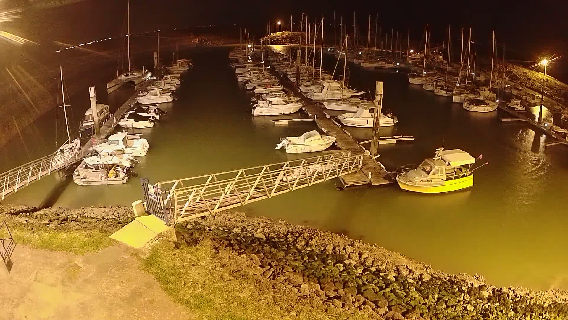 At night, numerous boats are docked at a marina, illuminated by artificial light.