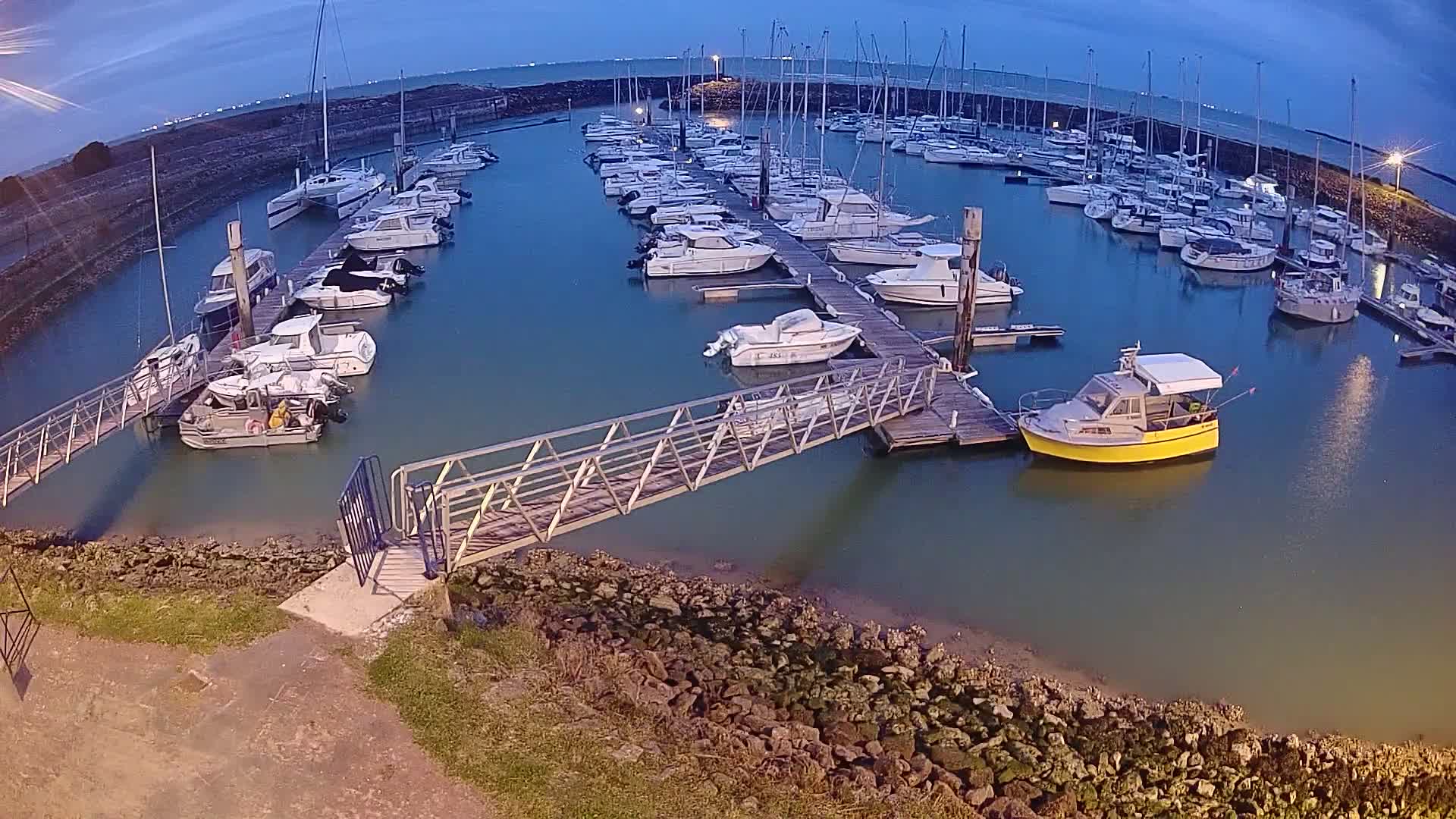 A marina filled with numerous boats of varying sizes is shown at dusk, under a twilight sky.