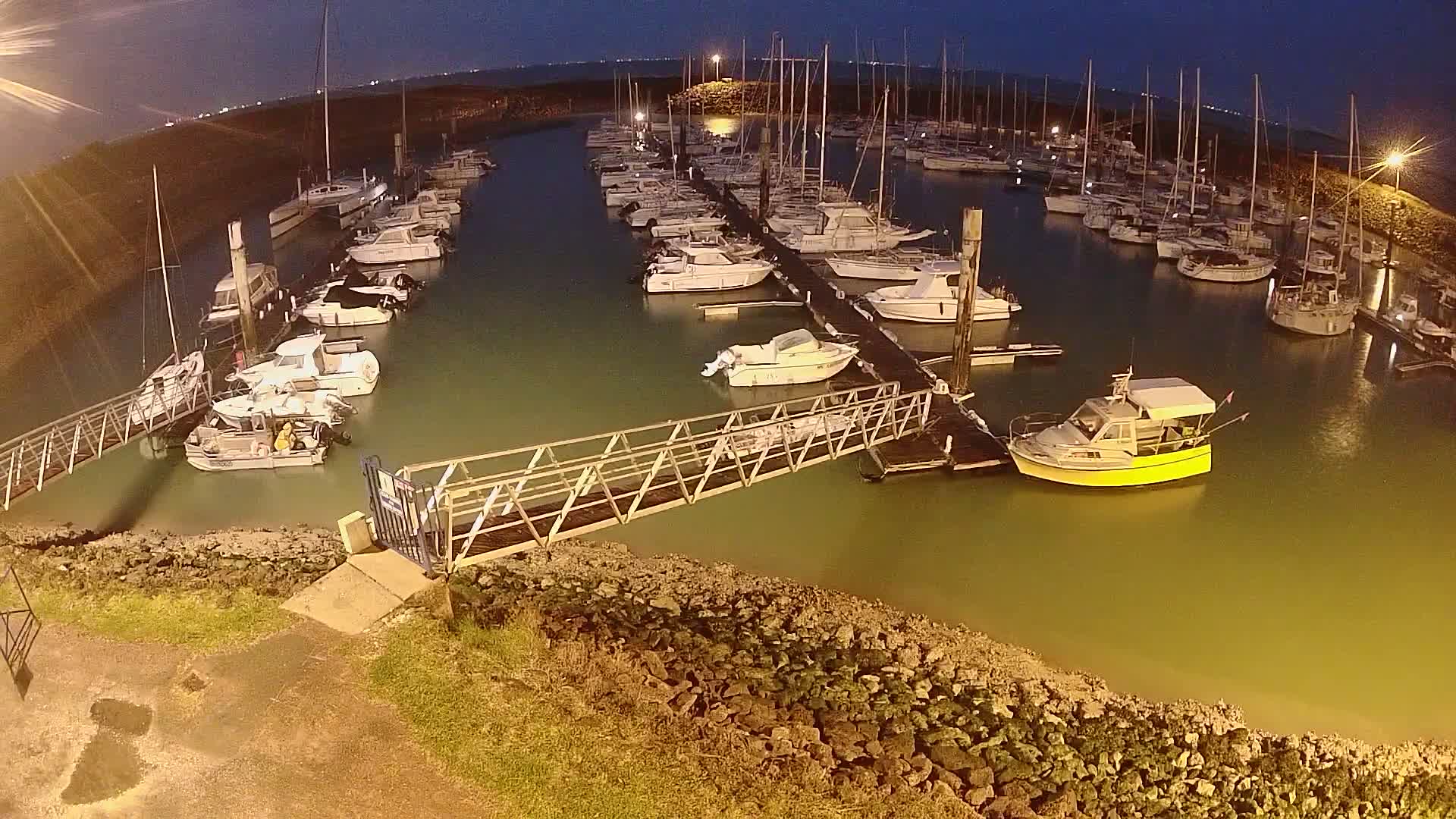 A marina at night, filled with numerous boats docked along piers, under a dark sky.