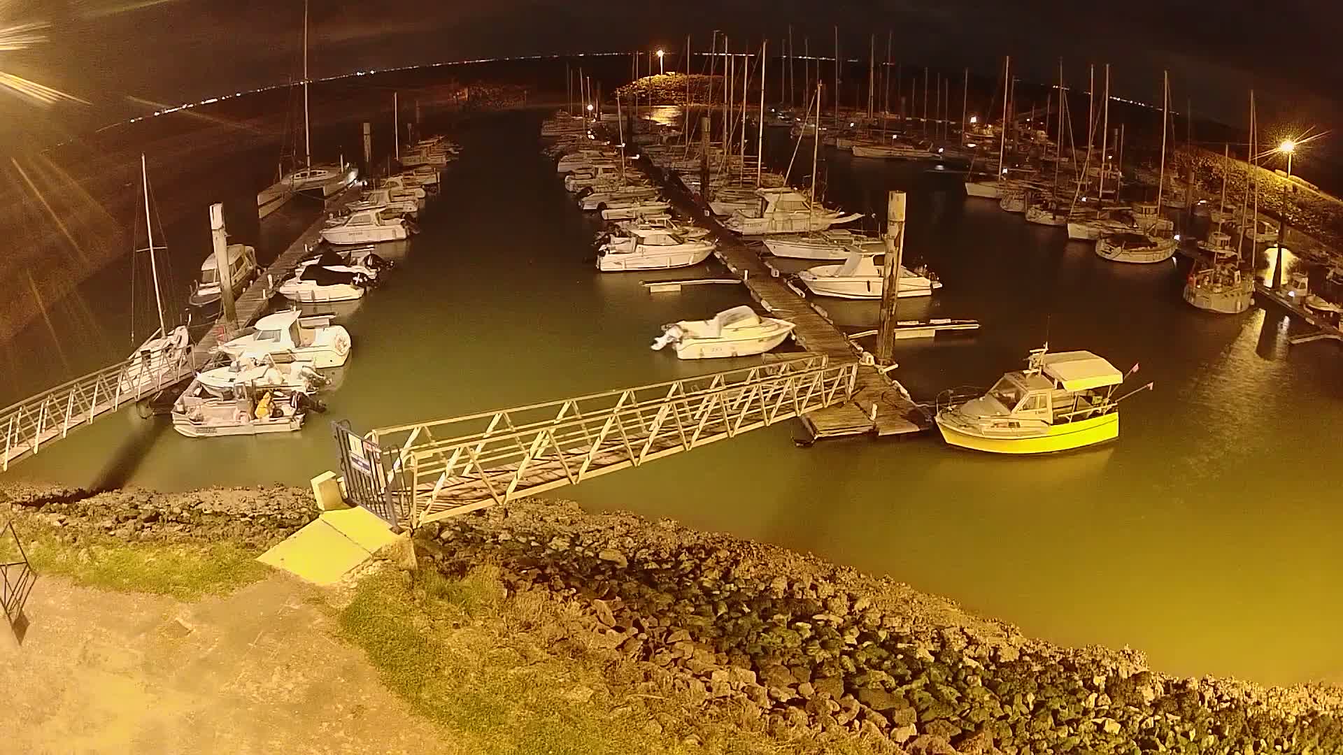 A marina at night, filled with numerous boats moored along docks, is illuminated under a dark sky.