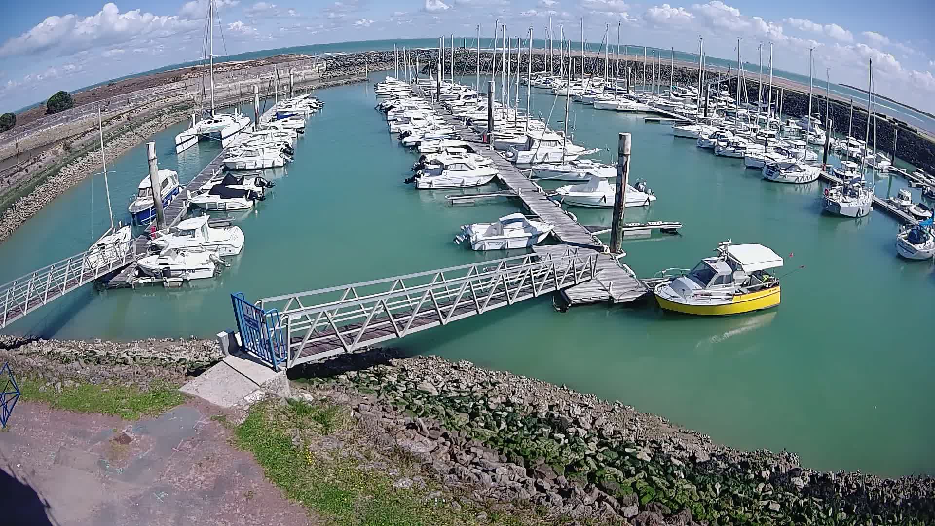 A marina filled with numerous sailboats and motorboats on a sunny day with partly cloudy skies.