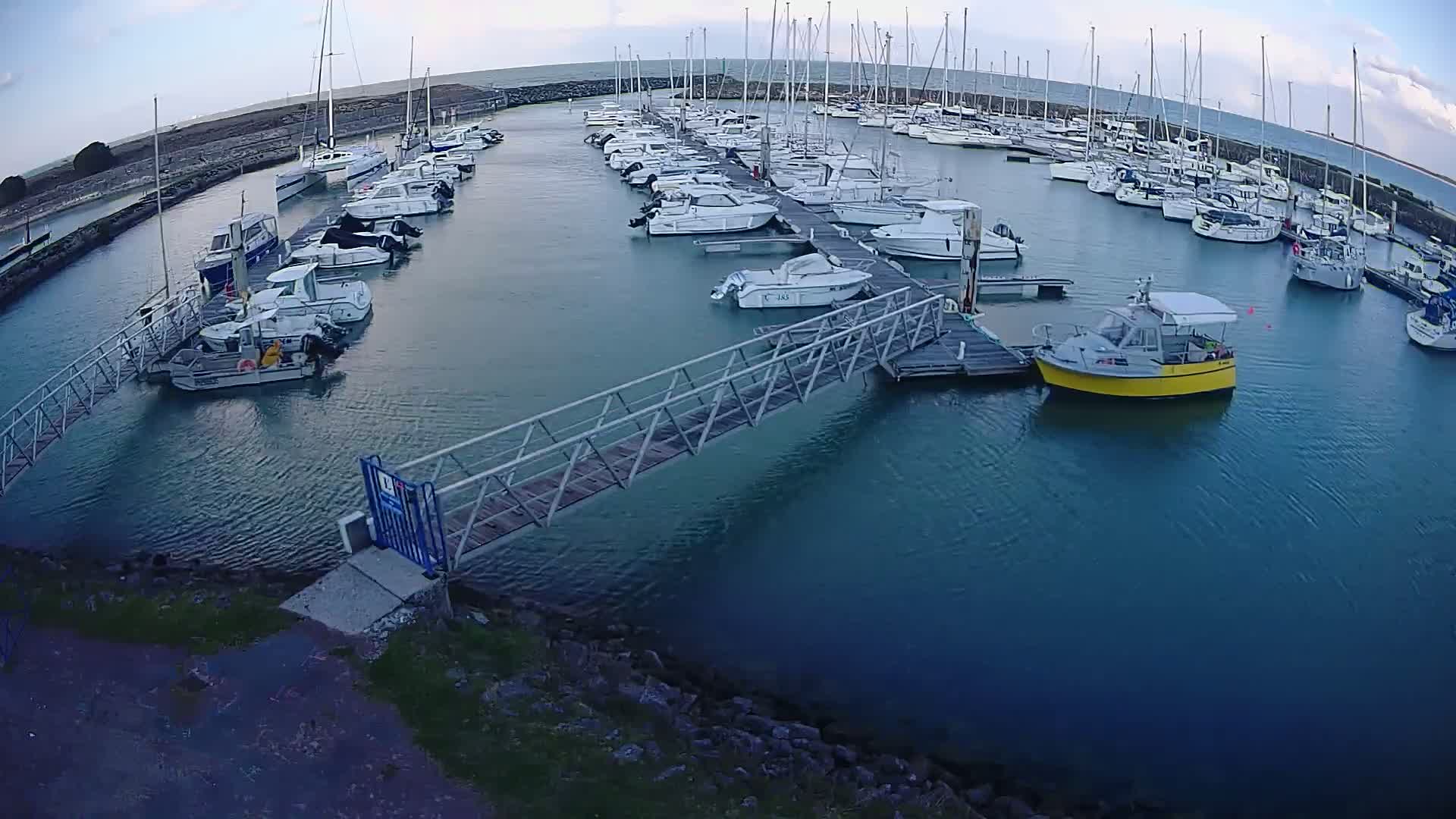 A marina filled with numerous sailboats and motorboats under a partly cloudy sky.