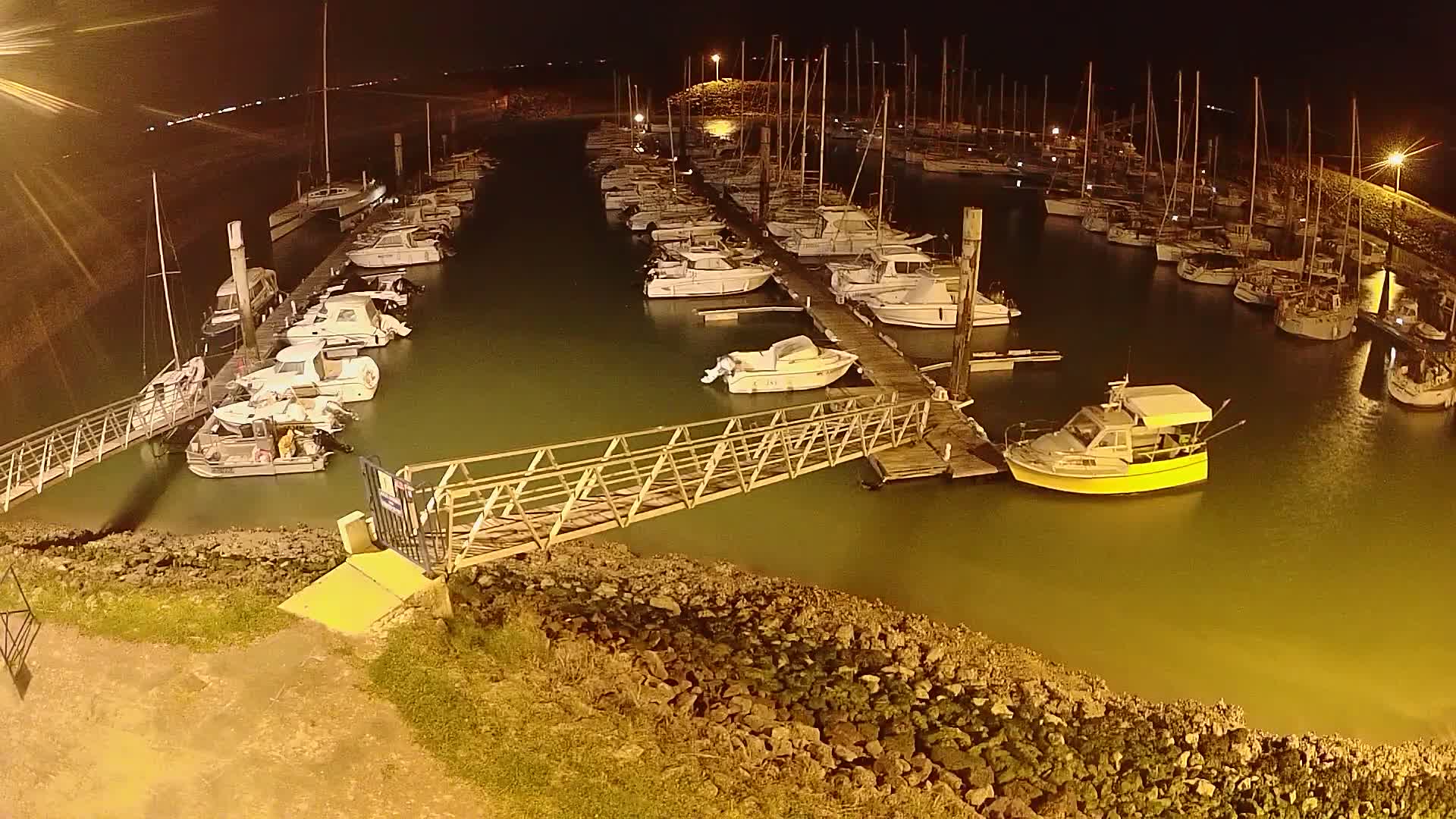 Many boats are docked at a marina at night, illuminated by artificial light.