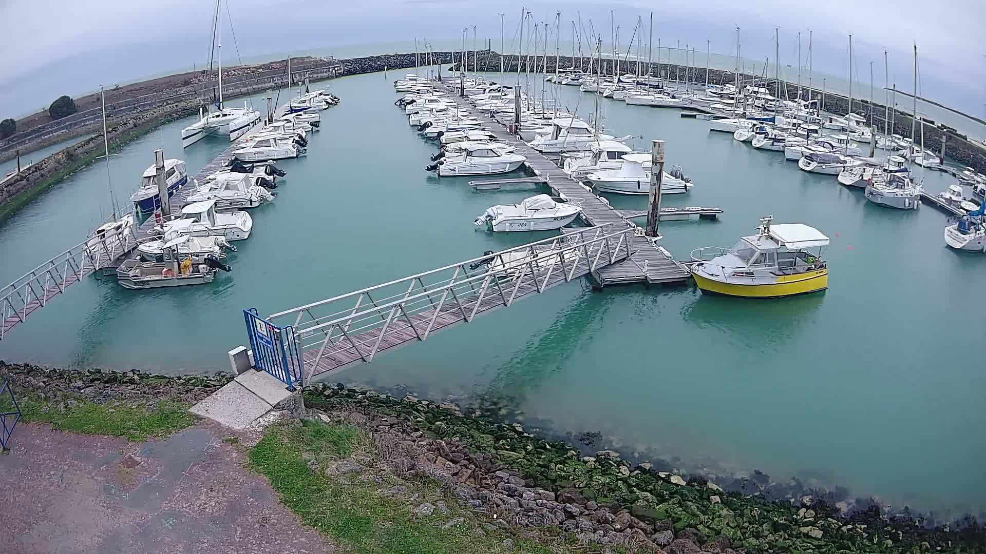 A marina filled with numerous boats on a cloudy day, with a metal walkway leading to a dock.