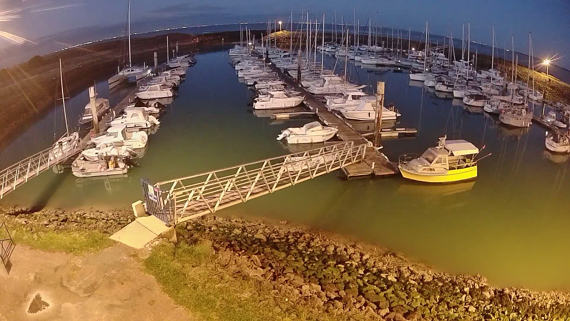 A marina at night, filled with numerous boats docked along piers, under a dark sky.