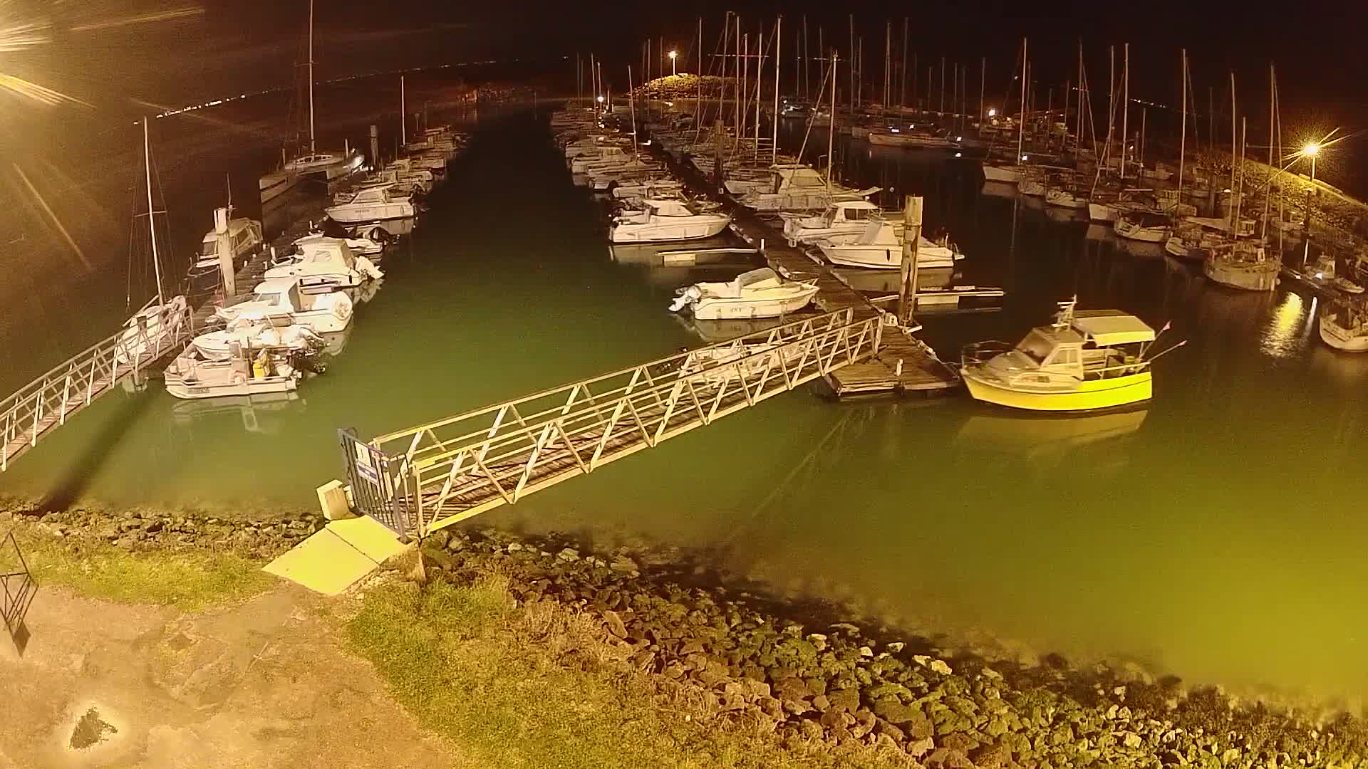 A marina at night, filled with numerous boats docked along piers, under a dark sky.