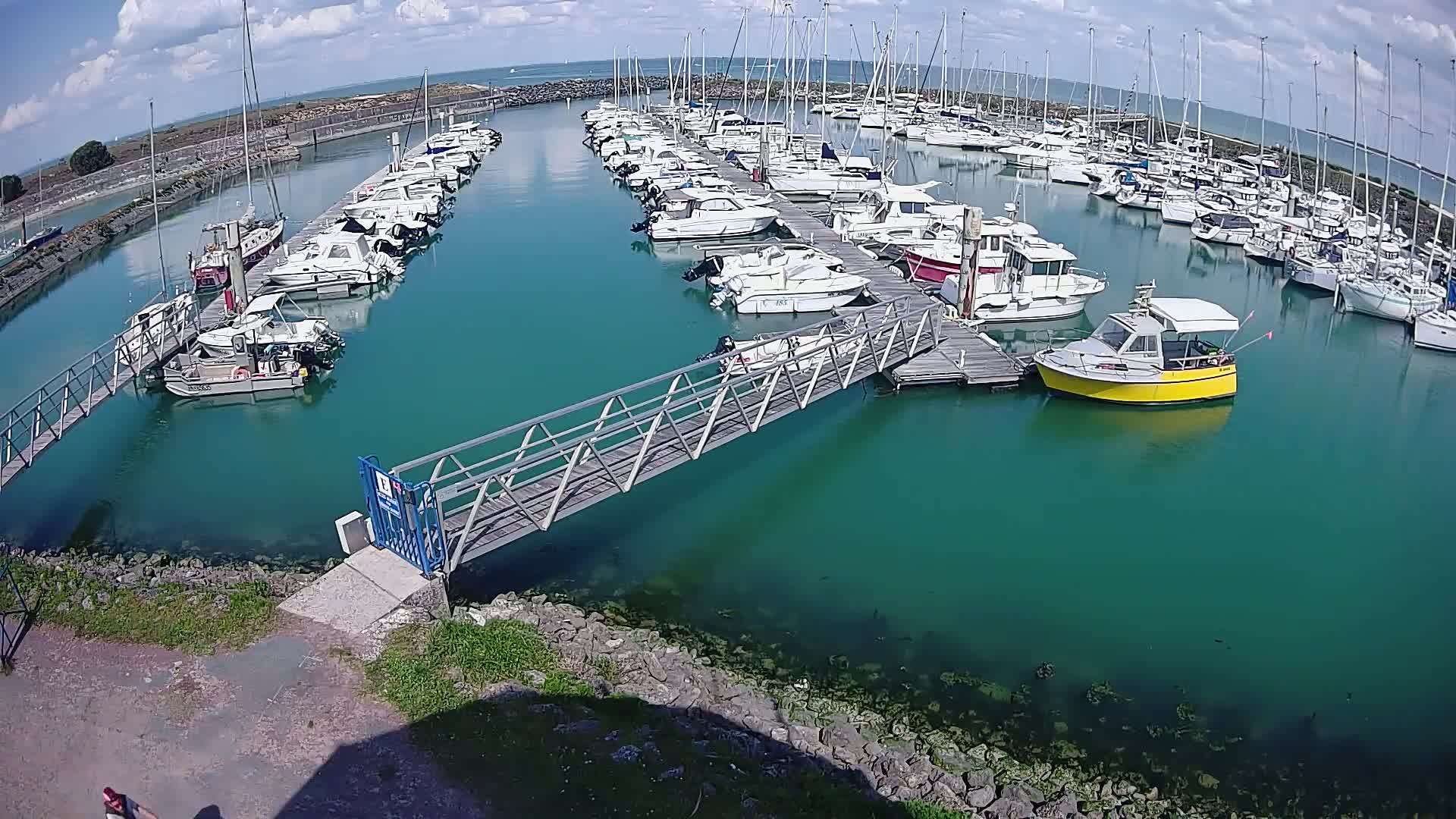 A marina filled with numerous sailboats and motorboats under a partly cloudy sky.