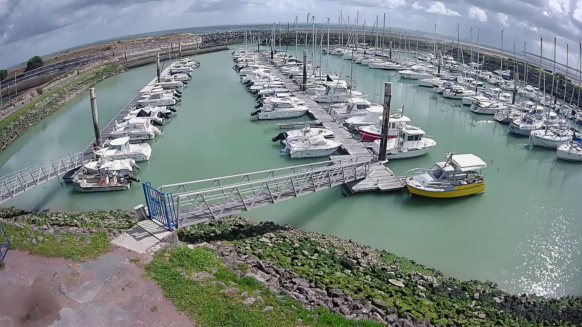 A marina filled with numerous boats of varying sizes is situated under a partly cloudy sky.